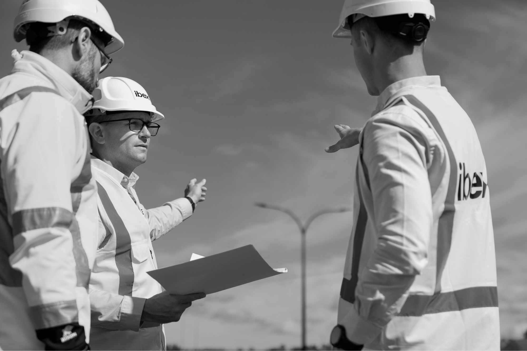 Three men in hard hats, working for ibex Lighting, are engrossed in a conversation.